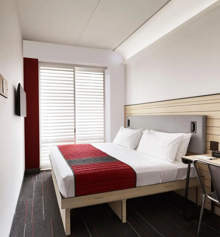 Une chambre d'hôtel moderne avec un grand lit recouvert d'une courtepointe rouge et grise.