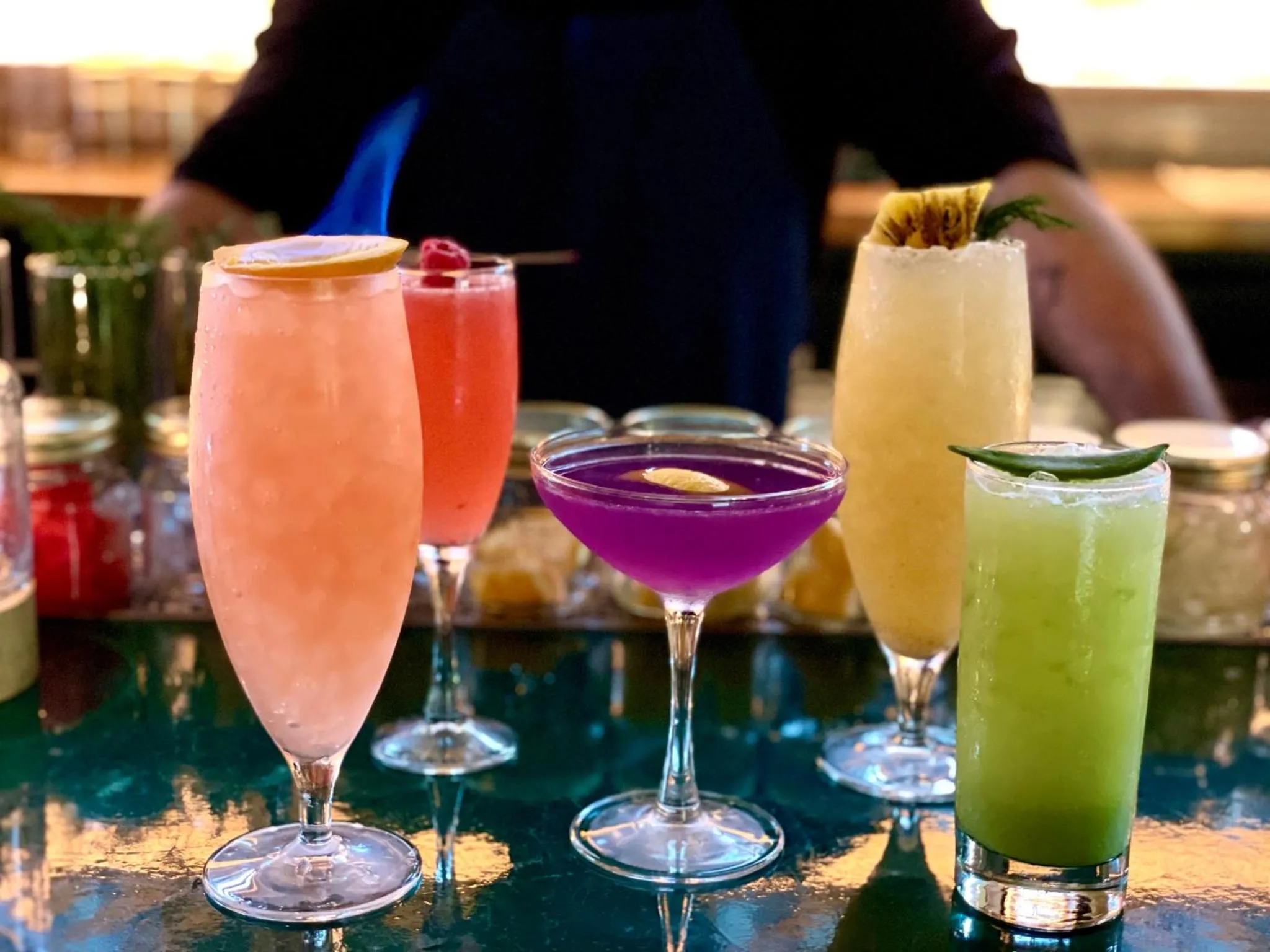Assortiment de cocktails colorés présentés sur un comptoir de bar.