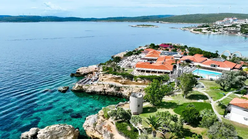 Vue aérienne d'un complexe hôtelier au bord de la mer avec piscine et végétation luxuriante.