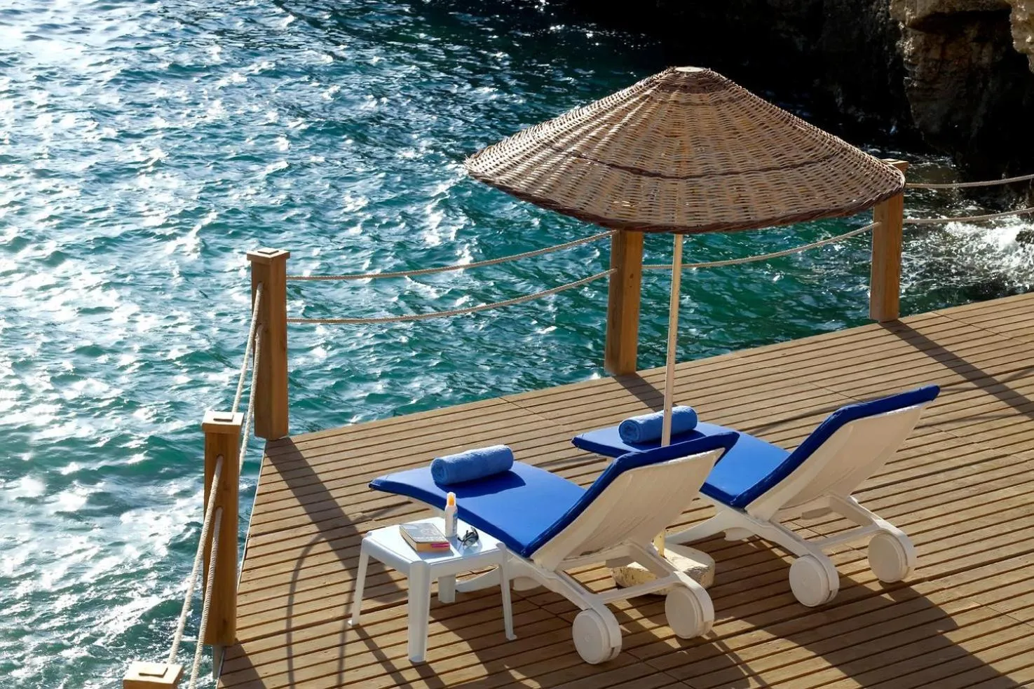 Transats bleus sur une terrasse en bois surplombant la mer.
