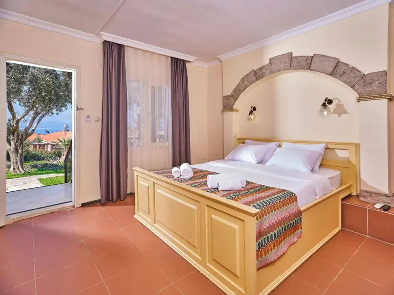 Chambre lumineuse avec un grand lit et une ouverture sur un jardin.