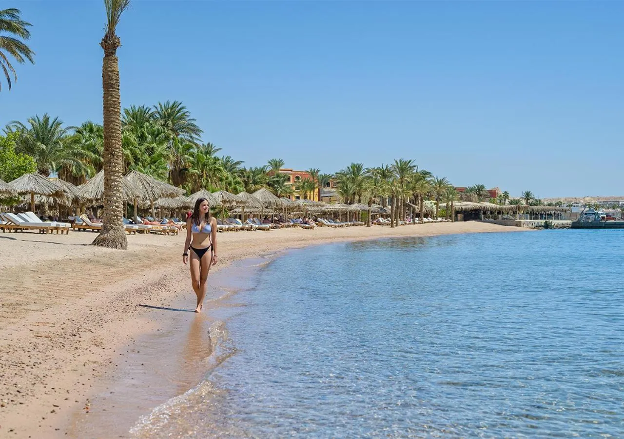 Une femme marche sur une plage de sable fin bordée de palmiers.