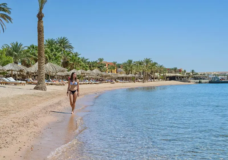 Une femme marche sur une plage de sable fin bordée de palmiers.