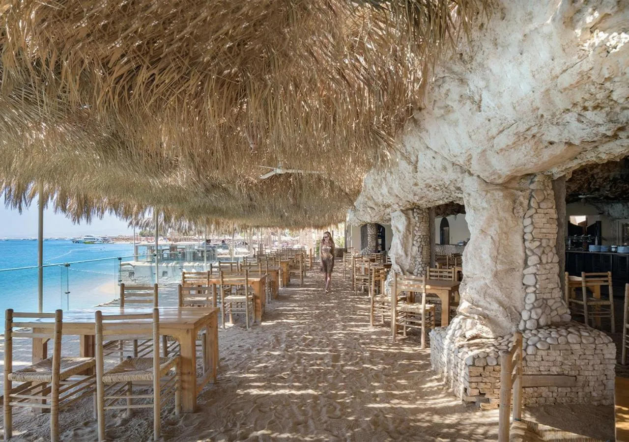Terrasse ombragée avec tables et chaises donnant sur la mer.