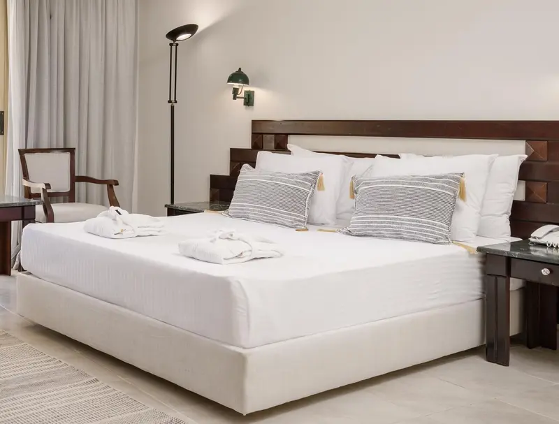 Une chambre lumineuse avec un grand lit recouvert de coussins et de couvertures blanches.