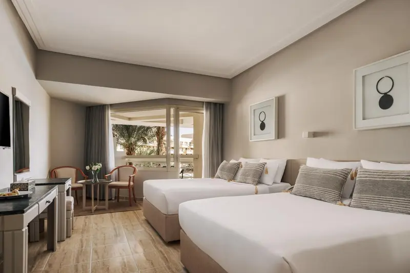Une chambre lumineuse avec deux lits simples et un fauteuil près d'une baie vitrée.