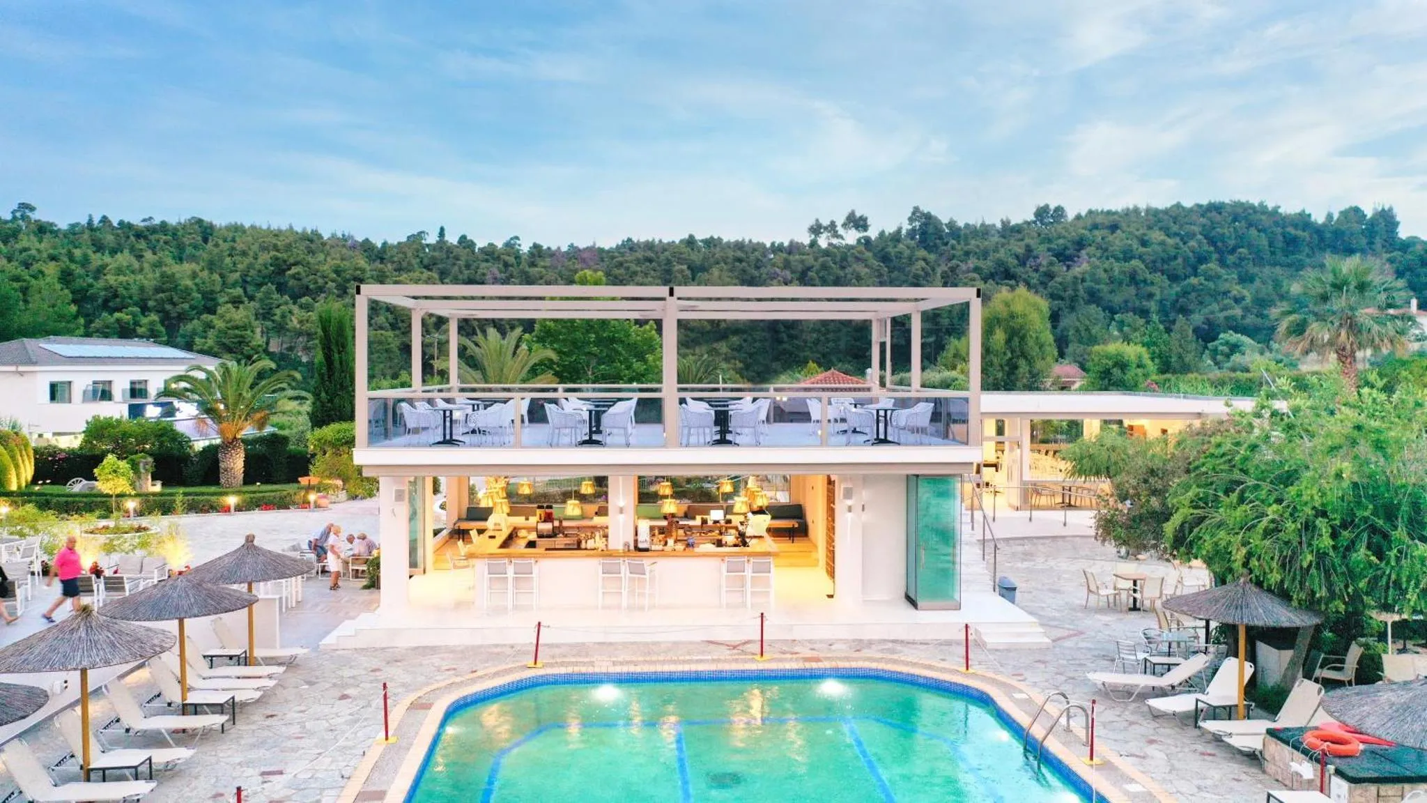 Bâtiment blanc moderne surplombant une piscine et une terrasse ombragée.