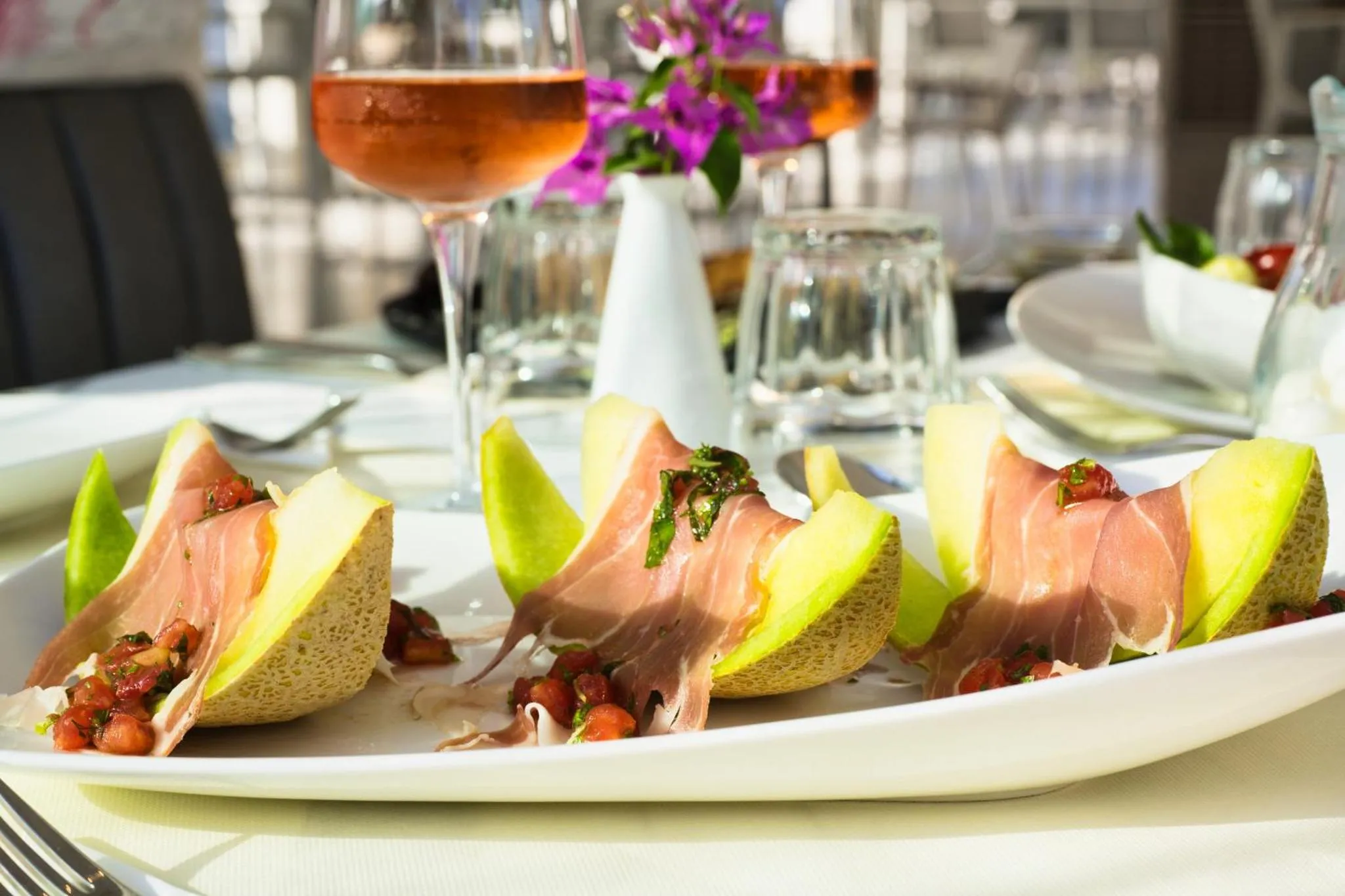 Assiettes de melon et jambon décorées de quelques herbes fraîches sur une table.
