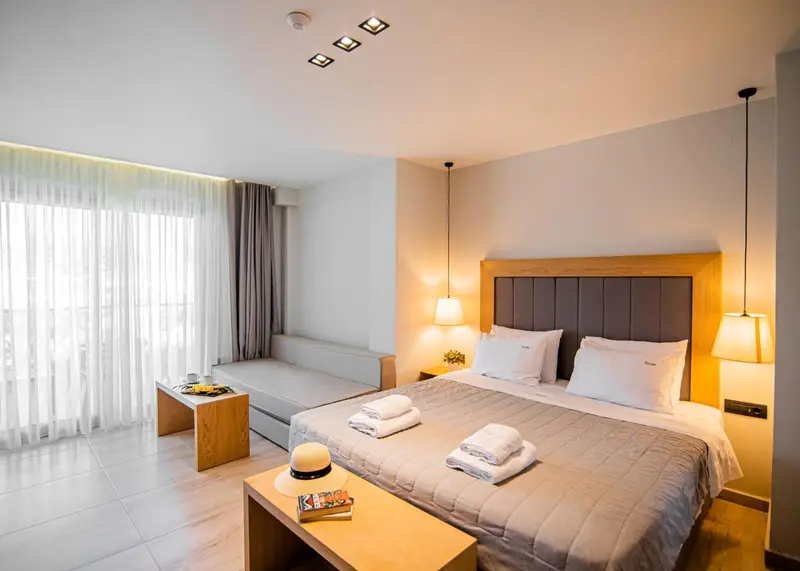 Chambre lumineuse avec un grand lit et un canapé près d'une fenêtre.