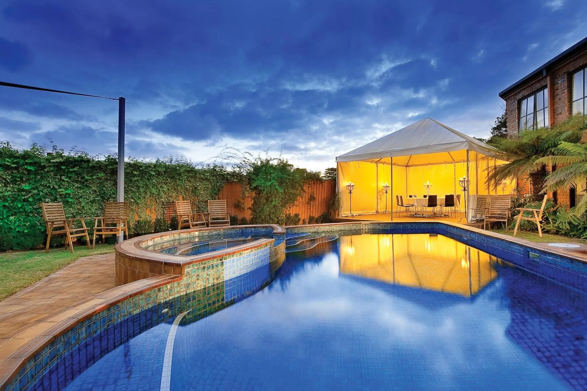 Piscine rectangulaire avec jacuzzi attenant, éclairée et entourée d'une végétation luxuriante.