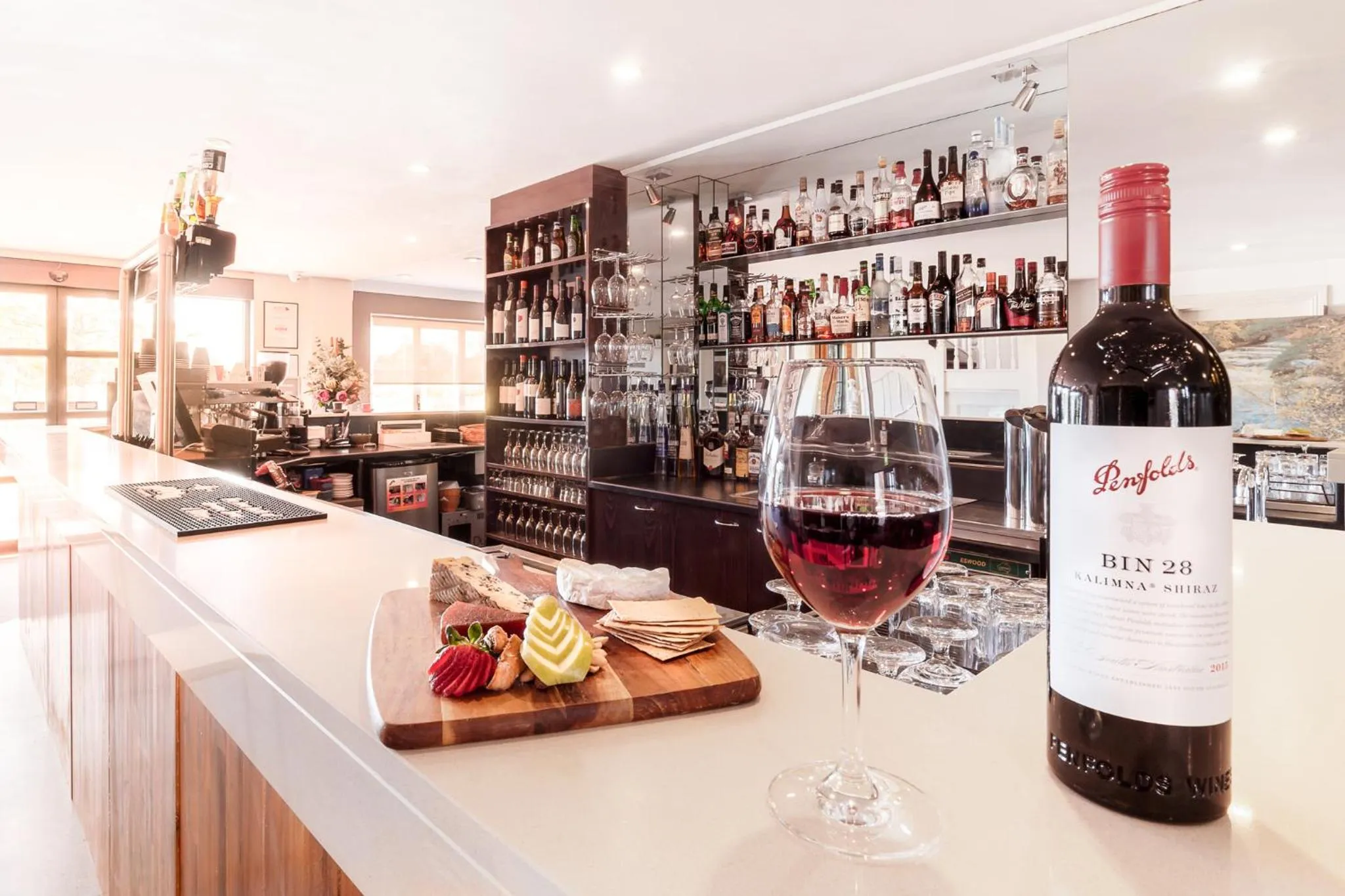 Un verre de vin rouge et une assiette de fromage sont servis sur un comptoir de bar bien garni.