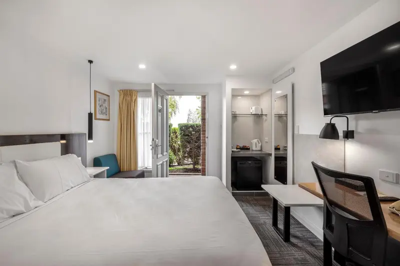 Chambre lumineuse avec un lit blanc et un bureau.