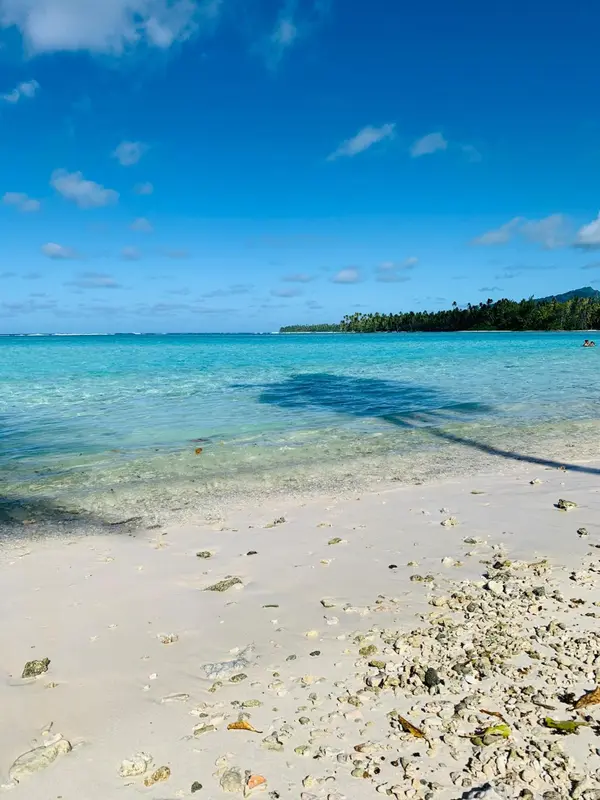 Plage de sable blanc bordée d'eau turquoise sous un ciel bleu nuageux.