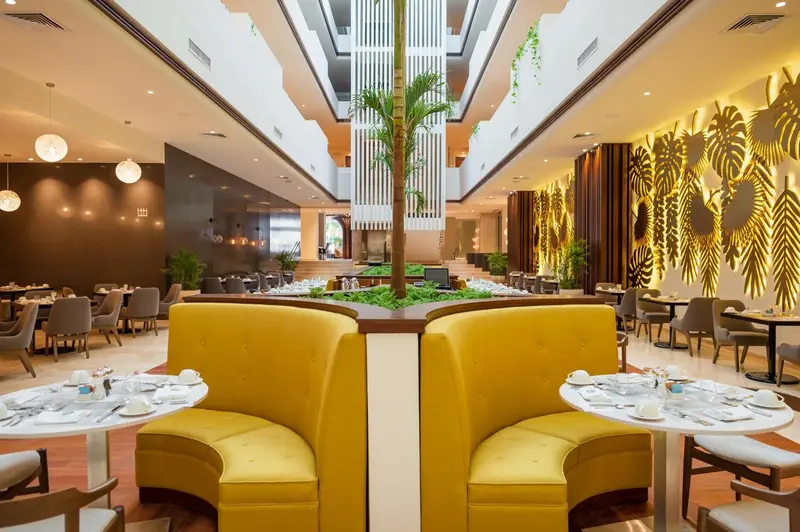 Une salle de restaurant lumineuse avec des tables dressées et des banquettes colorées.