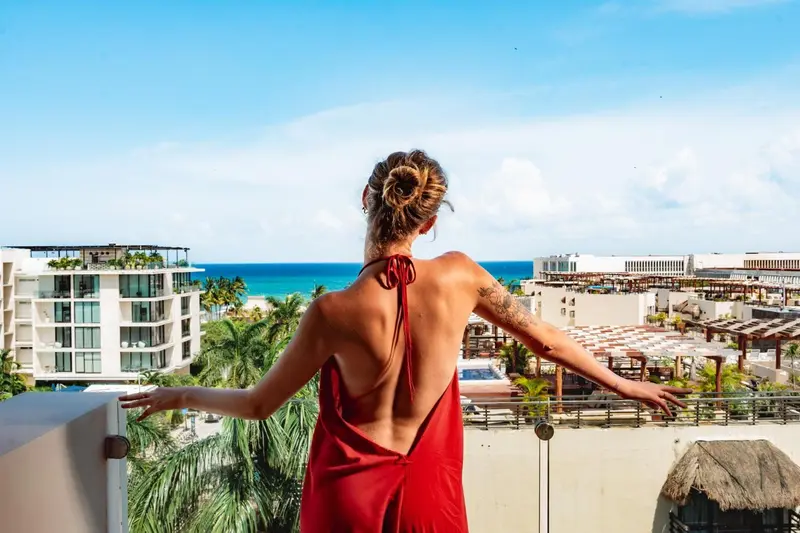 Une femme se tient sur une terrasse avec vue sur la mer et les bâtiments environnants.