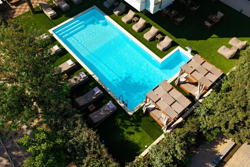 Vue aérienne d'une piscine rectangulaire entourée d'un solarium avec transats et parasols.