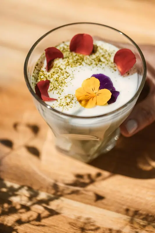 Un verre de boisson crémeuse décorée de fleurs et de poudre verte est posé sur une table en bois.