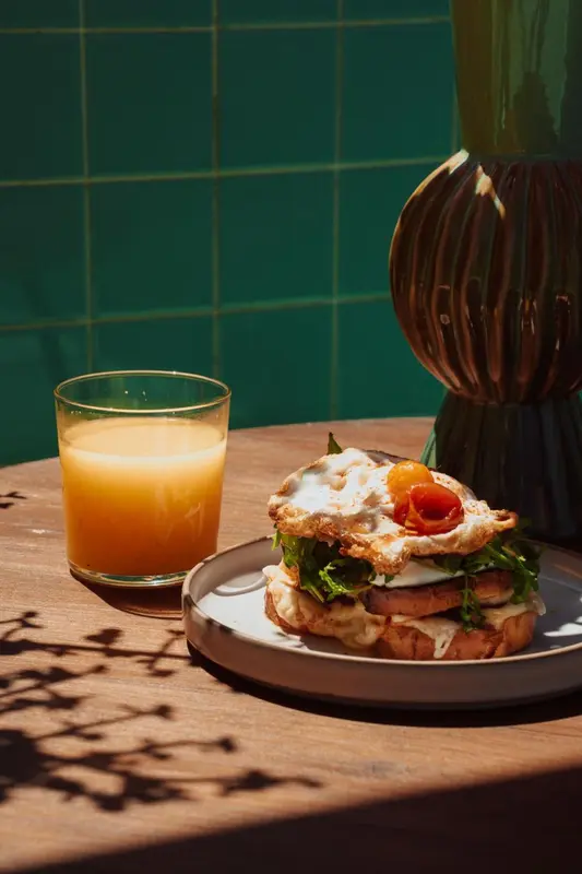 Un petit-déjeuner avec un jus d'orange et un sandwich aux œufs est présenté sur une table en bois.