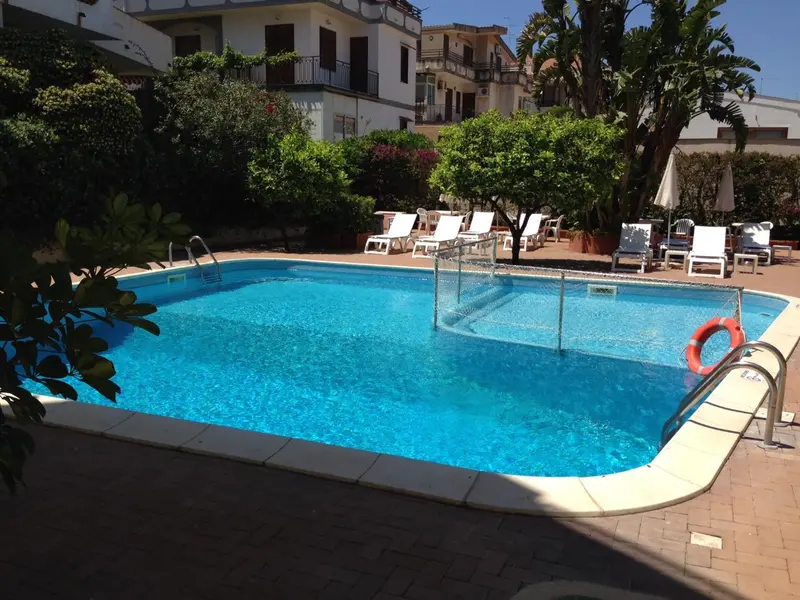 Une piscine rectangulaire bordée de chaises longues et de végétation luxuriante.