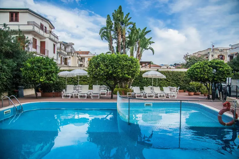 Transats blancs disposés autour d'une piscine bleue dans un jardin verdoyant.