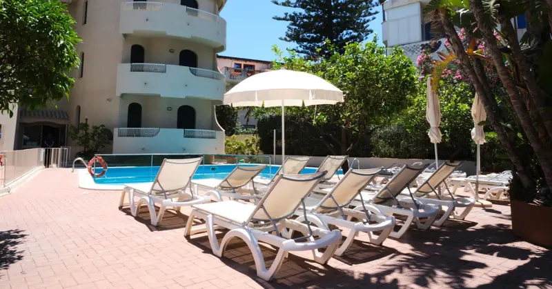 Transats blancs alignés au bord d'une piscine dans un jardin verdoyant.