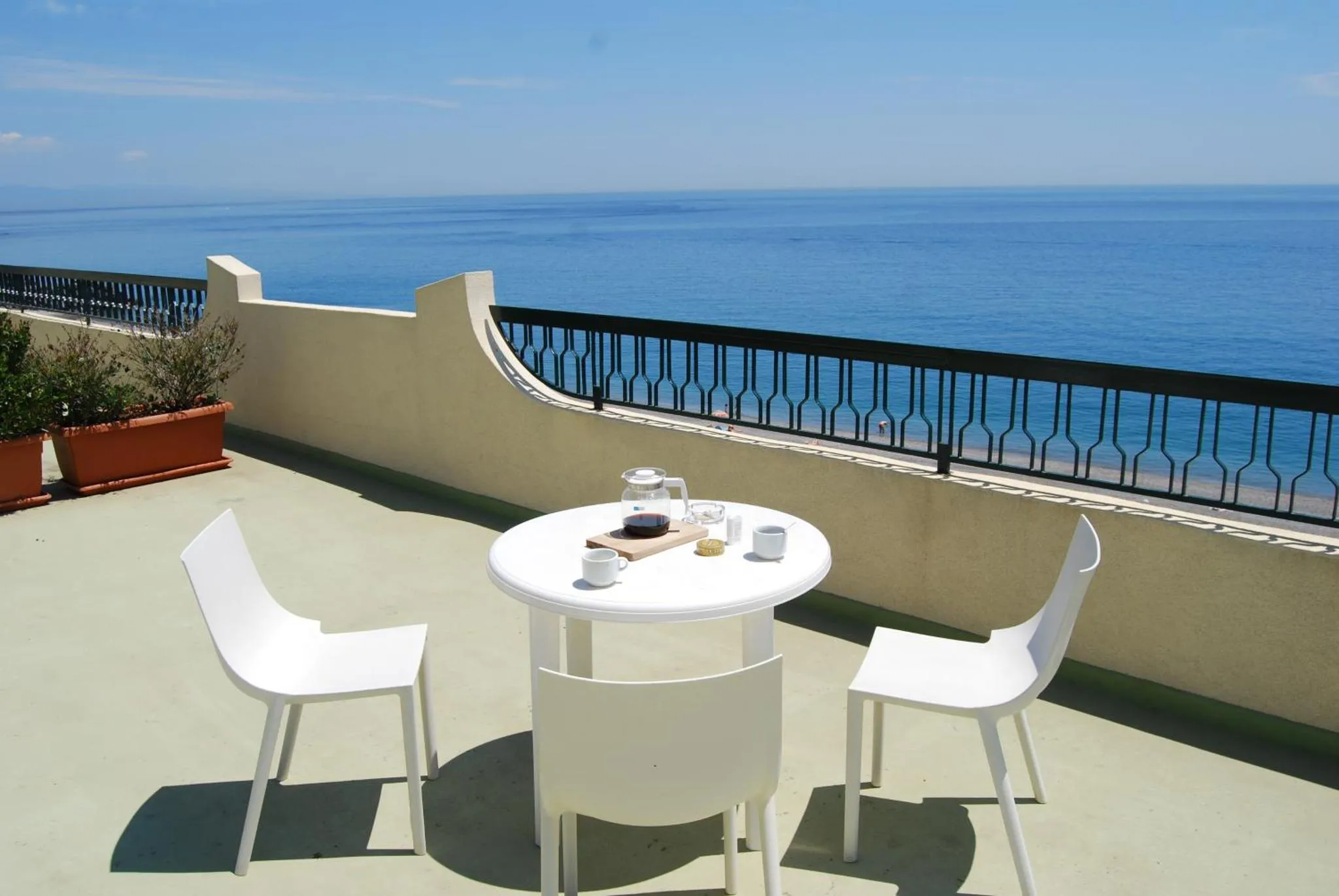 Une table et des chaises blanches sont disposées sur une terrasse avec vue sur la mer.