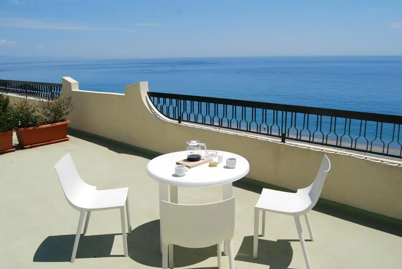Une table et des chaises blanches sont disposées sur une terrasse avec vue sur la mer.