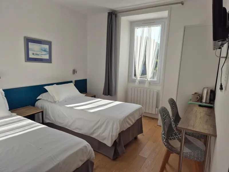 Une chambre lumineuse avec deux lits simples et un bureau près de la fenêtre.