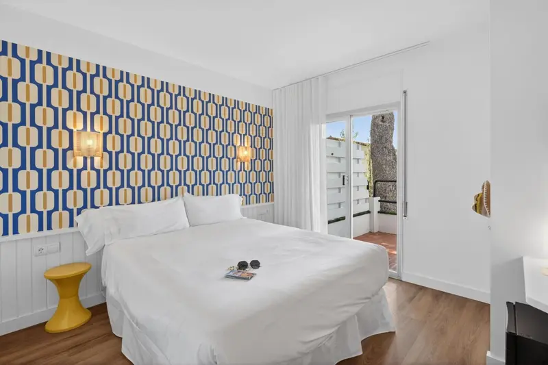 Une chambre lumineuse avec un grand lit recouvert de draps blancs et un mur décoratif.