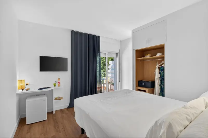 Chambre lumineuse avec un lit blanc et un bureau.