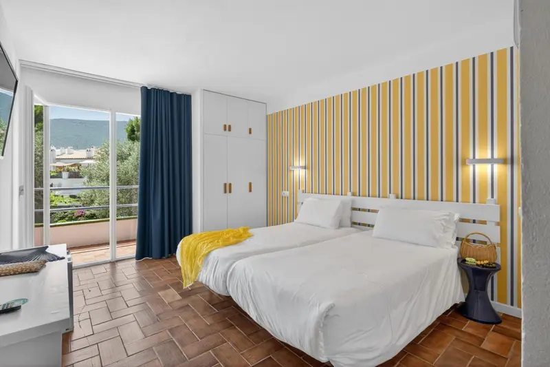 Chambre lumineuse avec un lit blanc et un mur rayé jaune et bleu.