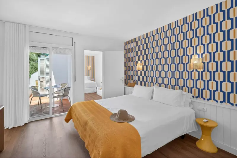 Chambre lumineuse avec un lit recouvert d'une couverture orange et un mur décoré de motifs géométriques.