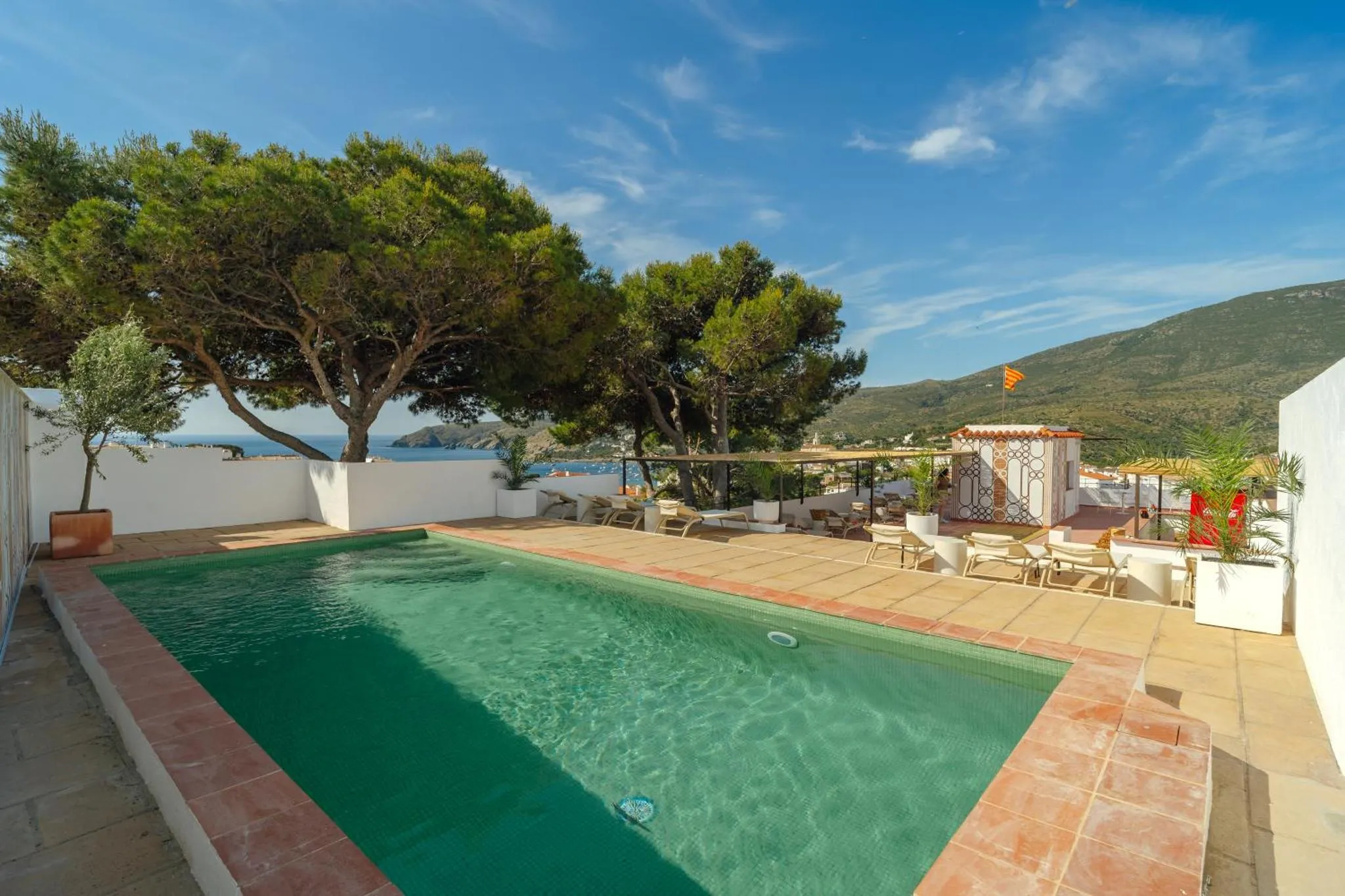 Une piscine rectangulaire avec une terrasse ensoleillée et une vue sur la mer.