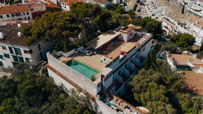 Vue aérienne d'un bâtiment blanc avec une piscine et des chaises longues sur le toit.