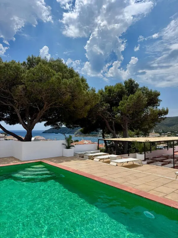 Une piscine turquoise bordée de transats blancs offre une vue sur la mer et le ciel nuageux.