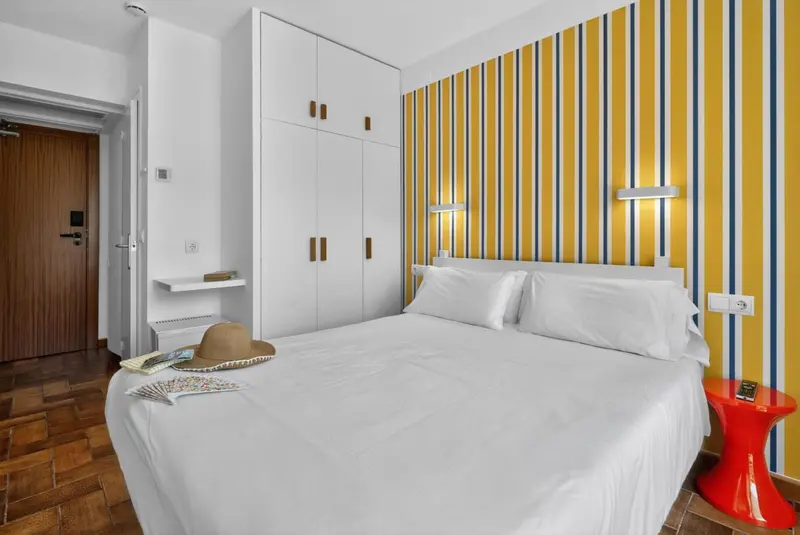 Une chambre lumineuse avec un grand lit recouvert de linge blanc et un mur rayé jaune et bleu.