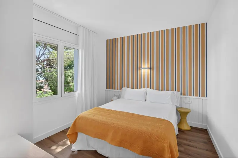 Une chambre lumineuse avec un lit recouvert d'une couverture orange et un mur rayé.