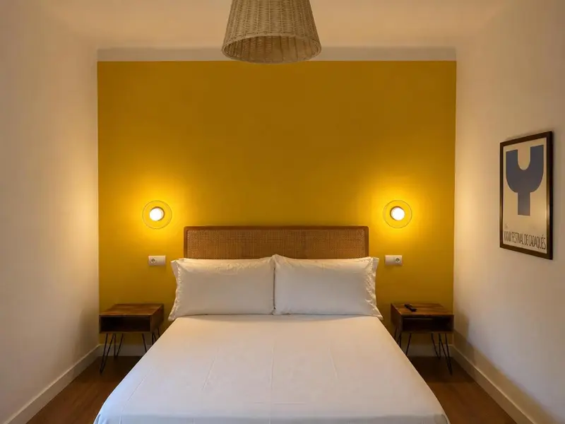 Une chambre lumineuse avec un grand lit et un mur jaune vif.