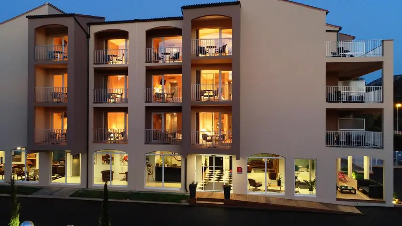 Façade d'un bâtiment avec des balcons éclairés et des tables.