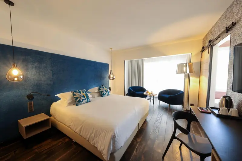 Une chambre lumineuse avec un grand lit et deux fauteuils.