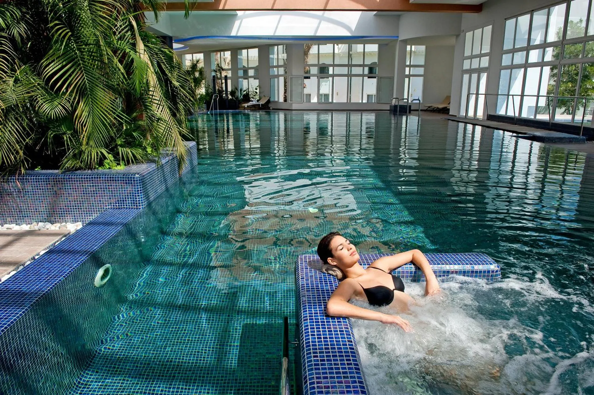 Une femme se détend dans une piscine intérieure lumineuse.