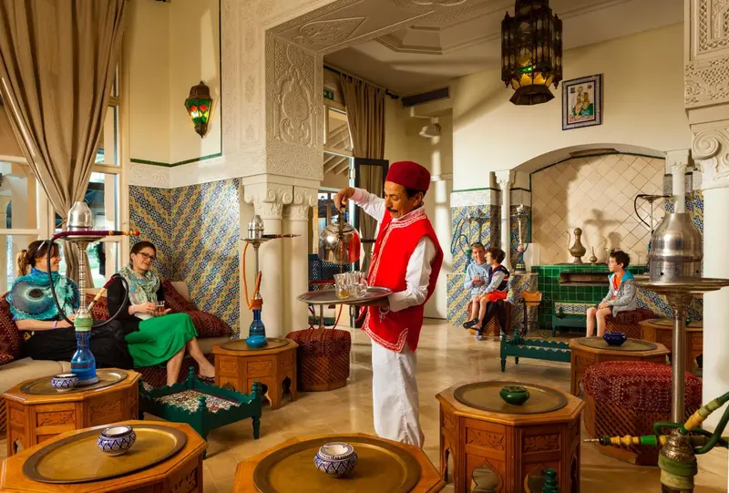 Un homme propose des thés et des narghilés dans un espace de détente décoré de motifs orientaux.