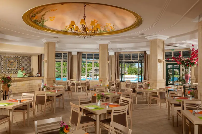 Une salle lumineuse avec des tables et des chaises, donnant sur une piscine et un jardin.