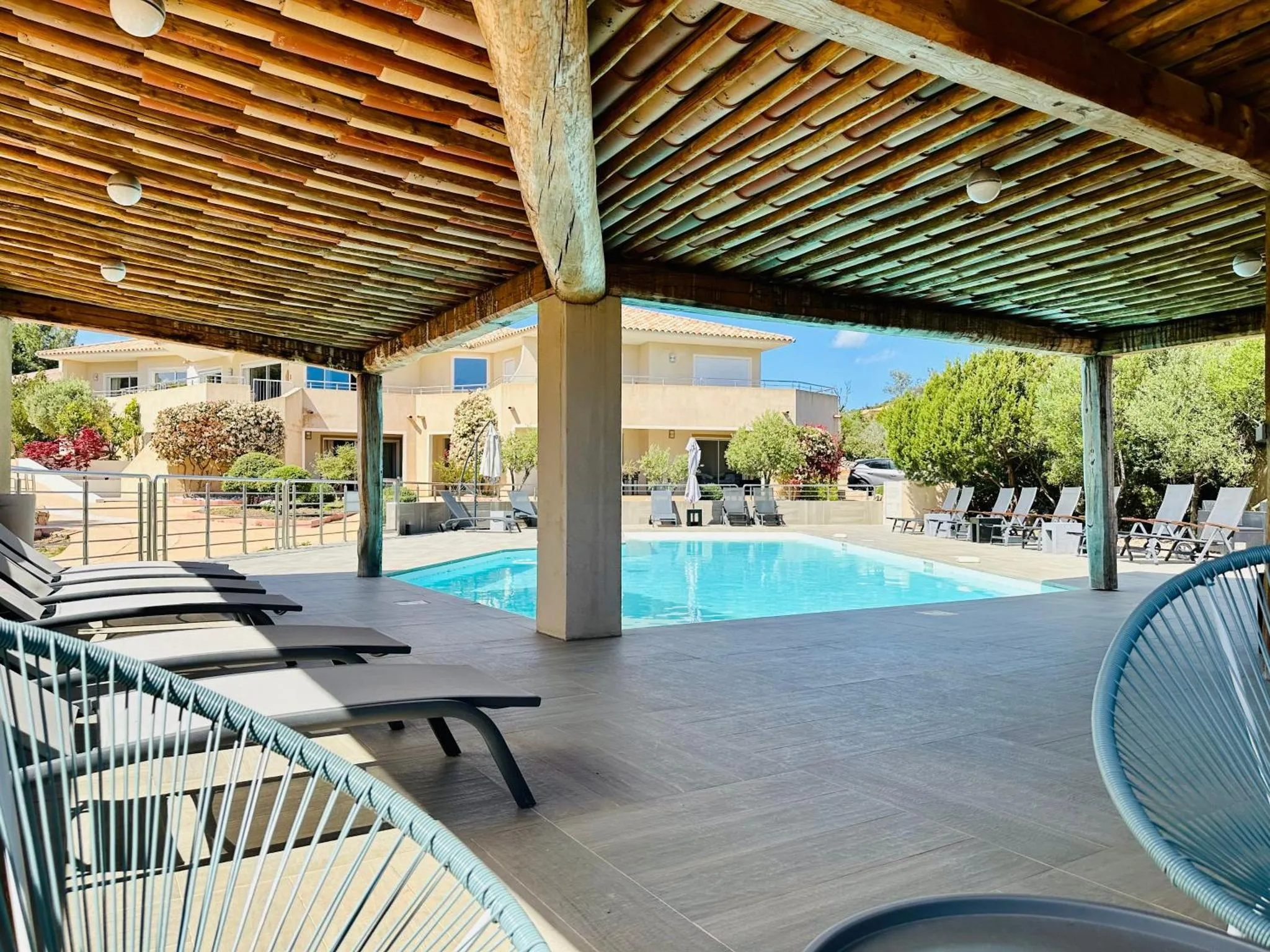 Transats bleus alignés devant une piscine ensoleillée sous une pergola en bois.