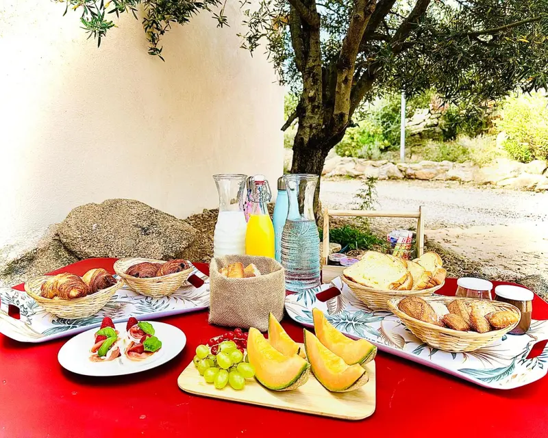 Une table rouge est dressée avec des viennoiseries, des fruits et des boissons.