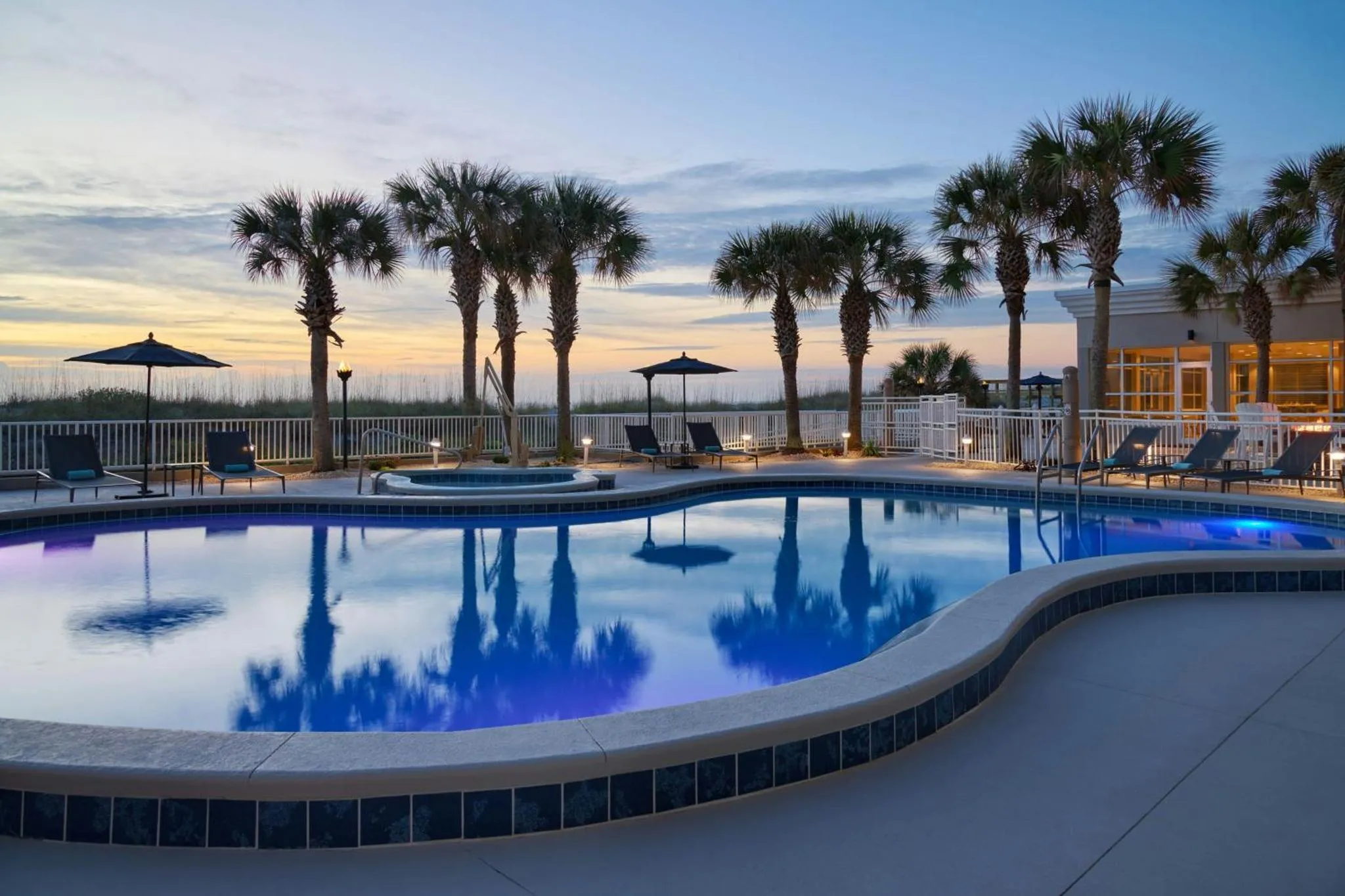 Piscine extérieure avec transats et palmiers au coucher du soleil.