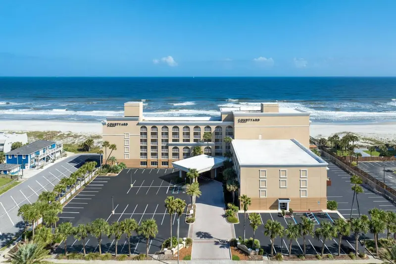 Vue aérienne d'un bâtiment beige et blanc avec un parking et une plage en contrebas.