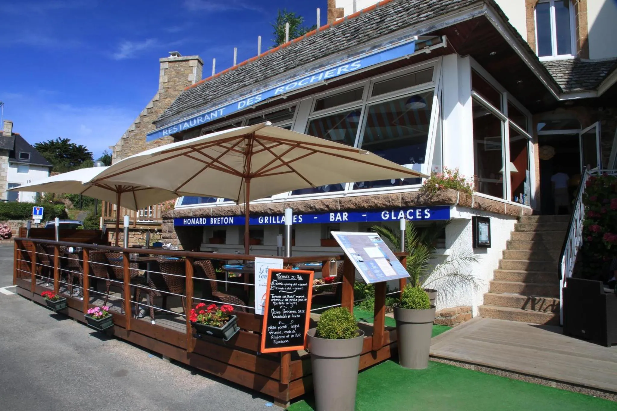 Terrasse ombragée avec tables et chaises devant un restaurant.