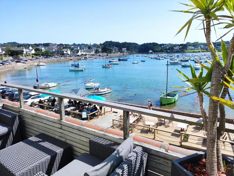 Terrasse en bois avec mobilier d'extérieur donnant sur un port de plaisance ensoleillé.