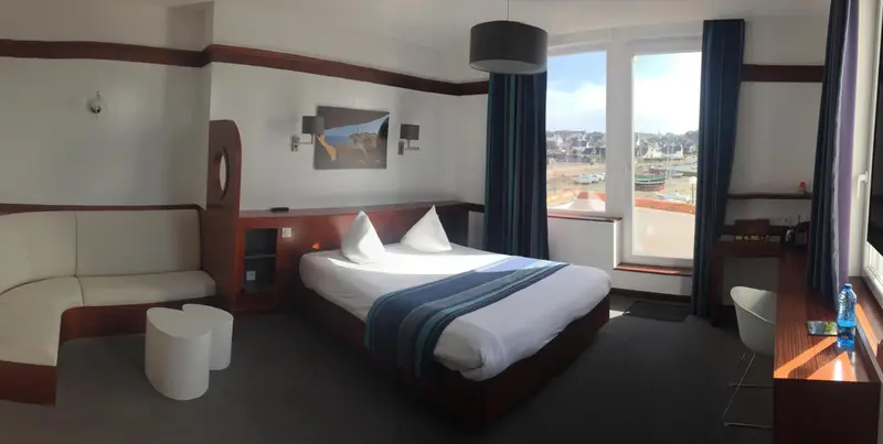 Chambre lumineuse avec un grand lit et un coin salon près d'une fenêtre.